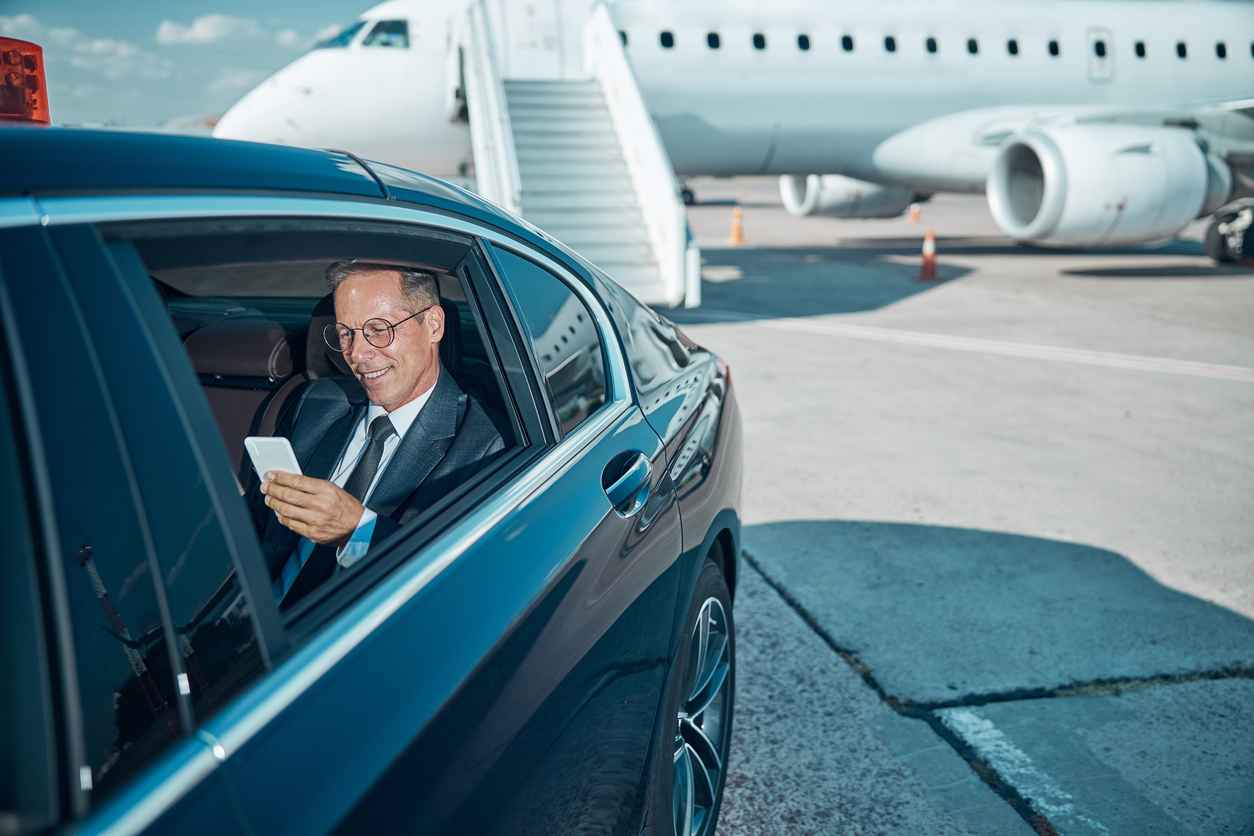Cheerful businessman with smartphone in car at airport