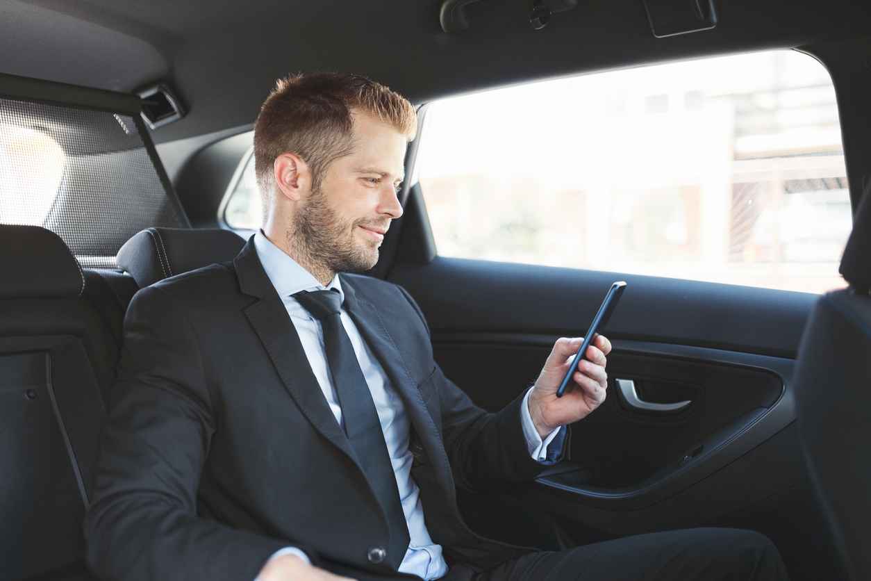 Executive businessman sitting at the back of car using a mobile phone